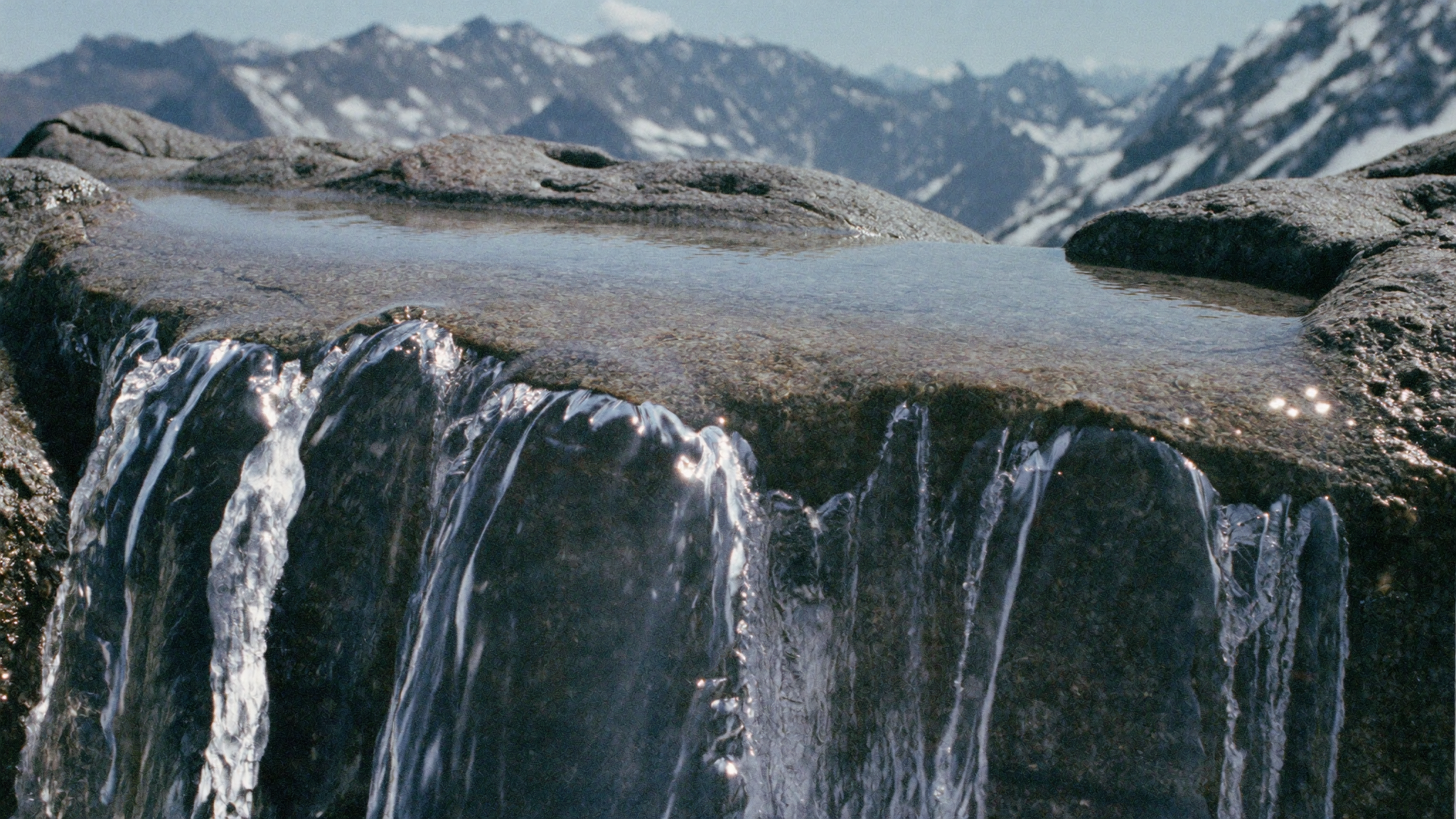 Crystal-clear alpine spring water flowing over granite stones in the Valais